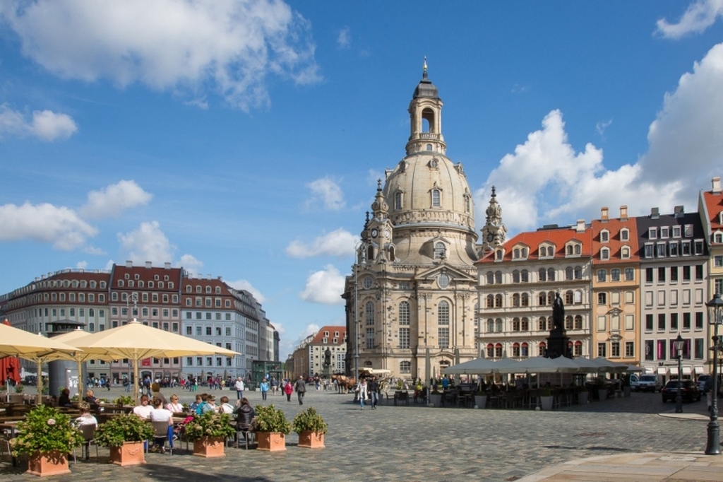 Die Frauenkirche in Dresden erhebt sich über den davor liegenden Marktplatz. Blauer Himmel, wenige Wolken