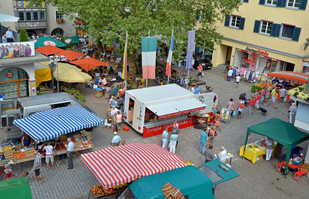 Marktplatz in Leutkirch von oben, eine Reihe von Verkaufsständen mit bunten Dächern sowie einige Passenten sind zu sehen