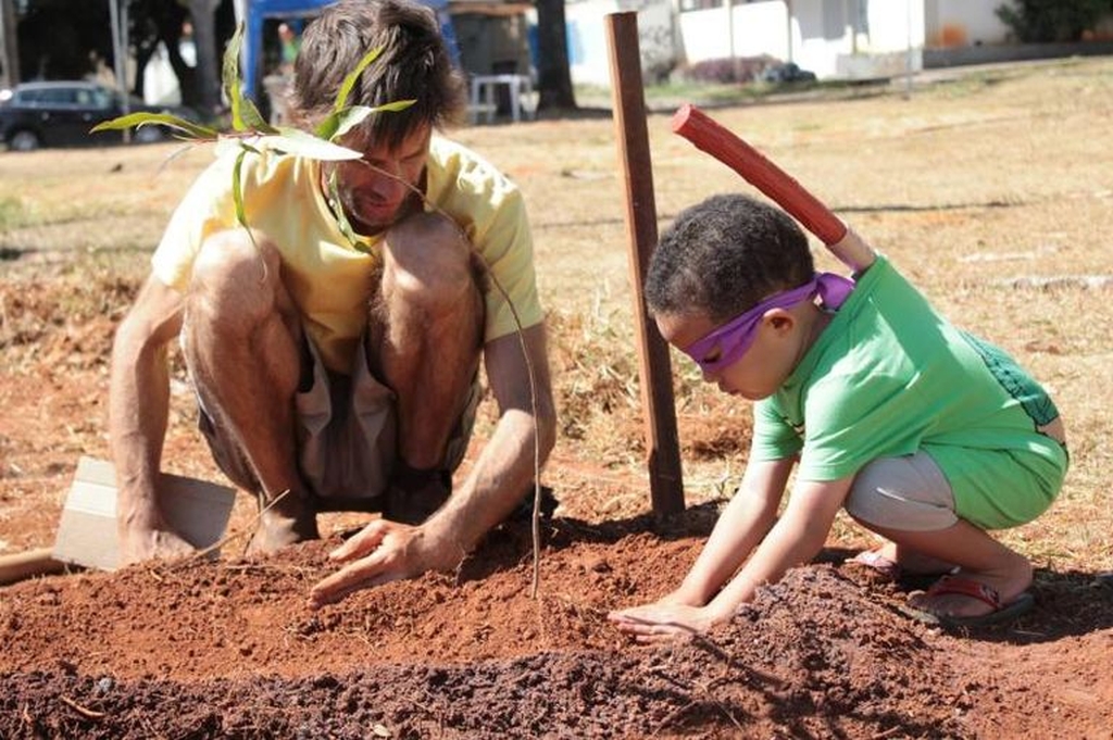 Ein Kind und ein Mann hocken nebeneinander auf erdigem Boden und graben eine Pflanze ein